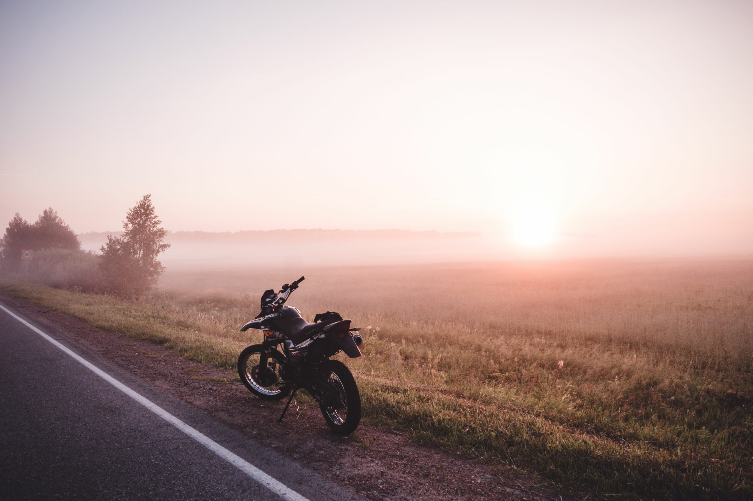 Une moto est dans le paysage et l'horizon, au bord d'une route, et un levé de soleil.