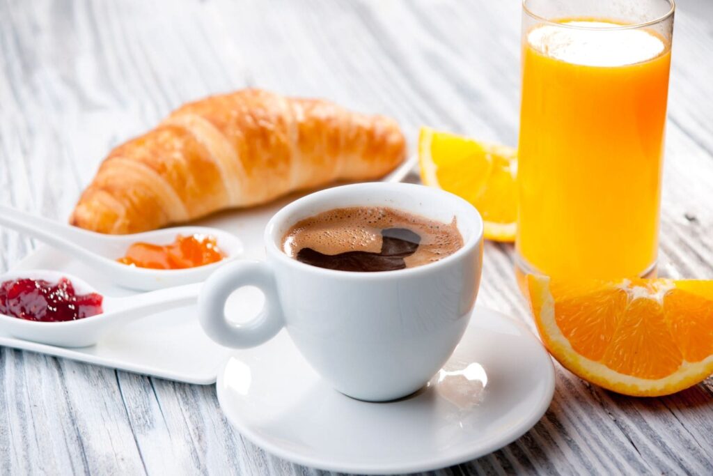 On voit une tasse de café, un croissant, la confiture, du jus d'orange.