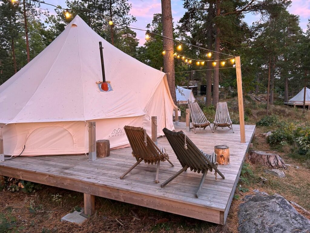 On voit une tente tipi en toile, sur une terrasse en bois avec un salon de jardin.